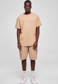 Tricou din bumbac bej, cu o croială relaxată și mâneci scurte, asortat cu șorturi cargo potrivite, dotate cu buzunare laterale și o croială lejeră.