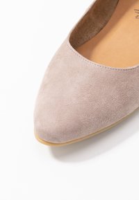 Zapato plano de ante gris con punta redonda, que presenta una textura suave y una suela de goma color marrón claro. Diseño minimalista, sin hardware visible.