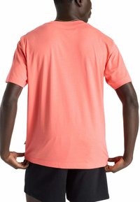 Camiseta de manga corta color coral en algodón suave, con cuello redondo y un corte relajado, combinada con pantalones cortos negros. Detalles de costura visibles.