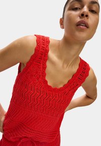 Rotes gehäkeltes Oberteil mit gewelltem Ausschnitt und strukturiertem Zickzack-Muster. Ärmelloses Design mit filigranen Durchbrüchen.