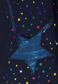 Toppa a forma di stella blu realizzata in materiale luccicante su un tessuto scuro, circondata da modelli di stelle colorate di varie dimensioni.