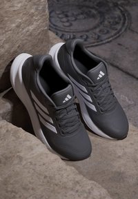 Paire de chaussures de sport noir et blanc avec lacets reposant sur des marches en pierre près d'une plaque d'égout métallique ronde.