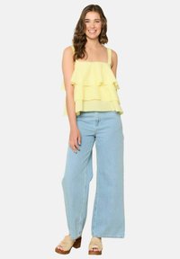 Rumena bluzica z nabrano obrobkom iz lahkega materiala s kvadratnim izrezom, v kombinaciji s svetloblue širokimi hlačami in bež platformskimi sandali.