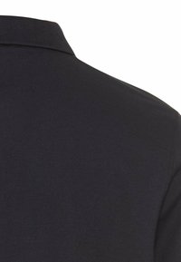 Sort polo skjorte med en tekstureret stof og en klassisk krave. Nærbillede som viser skuldersøm og stofdetaljer.