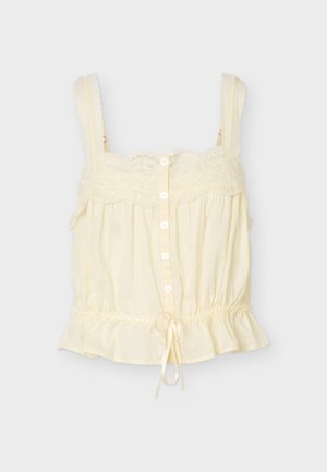 Κρεμ αμάνικο μπλουζάκι με διακοσμητική δαντέλα, κουμπιά μπροστά, ρυθμιζόμενους ιμάντες και σούρα στο τελείωμα με βολάν.