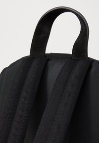 Sort rygsæk med tekstureret stof, der har to polstrede justerbare stropper og et robust håndtag i toppen for nem transport.