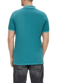 Teal polo tričko s krátkými rukávy a texturovaným povrchem, s límečkem a kontrastním lemem na rukávech a spodním okraji.