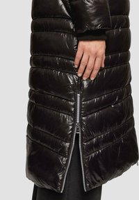 Schwarze Daunenjacke mit genähtem Muster, glänzender Optik und seitlichem Reißverschluss. Eigenschaften umfassen eine taillierte Silhouette und gerippte Bündchen.