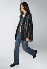 Zwarte leren blazer met twee voorzakken, gedragen over een gebreid sweater. Gecombineerd met blauwe straight-leg jeans en zwarte schoenen.