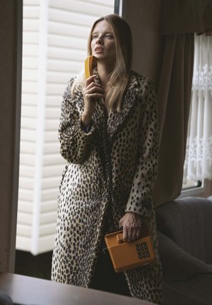 Płaszcz futrzany w panterkę z szerokim kołnierzem, trzymający jaskrawożółty, vintage telefon. Tekstura futra jest miękka, kontrastująca z gładkim wzorem telefonu.