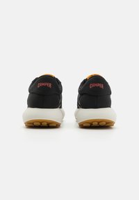 Schwarze Sneakers mit orangefarbenen Akzenten, ausgestattet mit einem strukturierten Obermaterial, einer weißen Zwischensohle und einer gummierten Außensohle mit kreisförmigen Profilmustern.