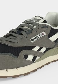 Γκρίζο και μαύρο αθλητικό παπούτσι Reebok με λευκές ρίγες, γκρίζα κορδόνια και μπεζ σόλα, με το λογότυπο και τη σημαία Union Jack στο πλάι.