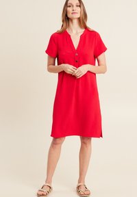 Rotes, kurzärmliges Kleid mit tiefem V-Ausschnitt, drei Knöpfen vorne und einer lockeren Passform mit seitlichen Schlitzen. Glatte Stofftextur.