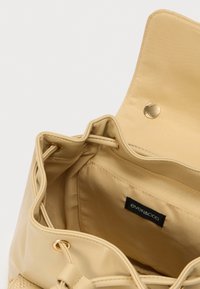 Μπεζ τσάντα χειρός με απαλή, λεία υφή, διαθέτει εσωτερική επένδυση και κλείσιμο με μαγνητικό κουμπί. Περιλαμβάνει μαύρη ταμπέλα με το λογότυπο εσωτερικά.