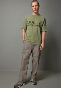 Oliven grøn bomulds t-shirt med sort trykt tekst; parret med løstsiddende beige cargo bukser med sidelommer og en glat tekstur.