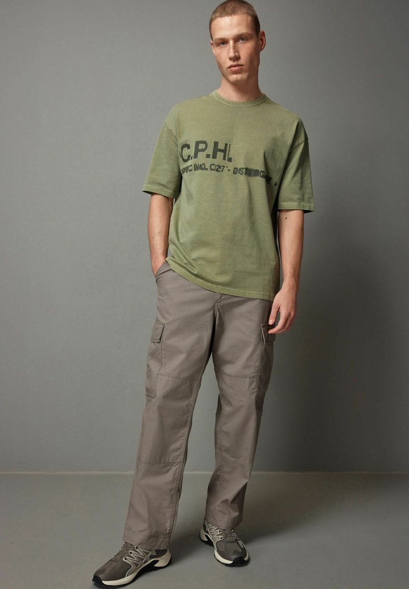 Oliven grøn bomulds t-shirt med sort trykt tekst; parret med løstsiddende beige cargo bukser med sidelommer og en glat tekstur.