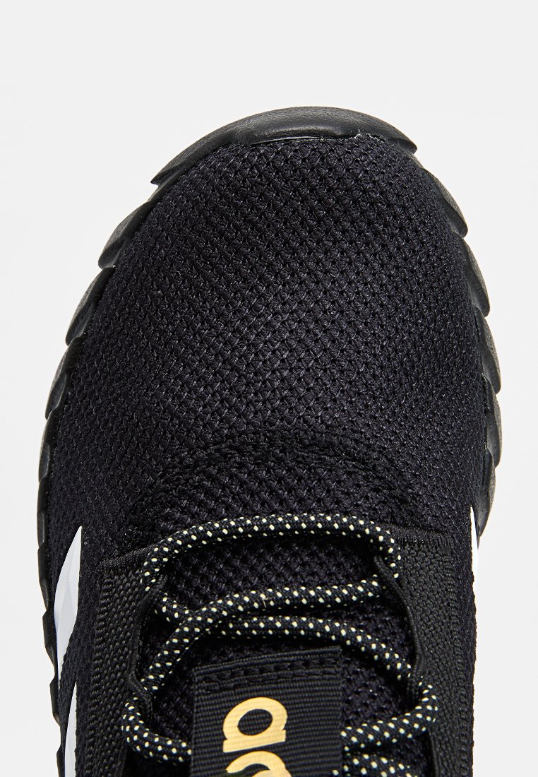 Zwarte sportieve schoen met ademend mesh bovenwerk, gestructureerd oppervlak, reflecterende accenten en contrasterend wit logo. Beschikt over patroonveters.