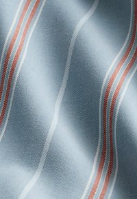 Tejido de color azul claro con una textura suave, que presenta rayas onduladas en blanco y rojo. La trama es apretada, mostrando detalles de costura.