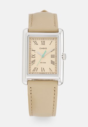 Casio rechteckige silberne Uhr mit beigem Lederarmband, cremefarbenem Zifferblatt, römischen Ziffern und drei blauen und silbernen Zeigern, die 1:09:35 anzeigen.