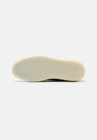 Black shoe sole with a smooth, translucent finish and light beige rubber details. Features a textured pattern for traction.