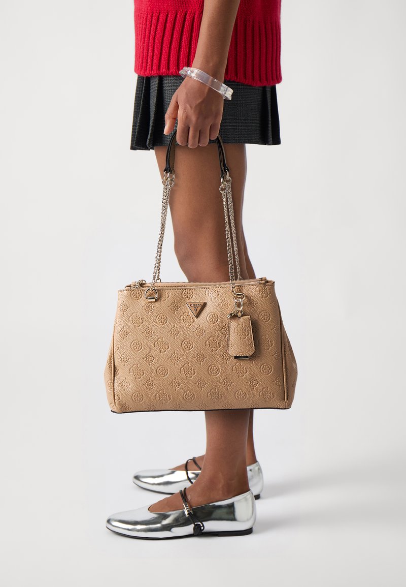 Borsa a tracolla in ecopelle marrone con motivo a rilievo, cinturino a catena e un piccolo etichetta. Abbinata a scarpe flat argentate e un maglione rosso.