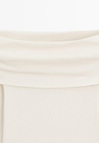 Bluzka w kolorze ecru z drapowanym, złożonym dekoltem, wykonana z gładkiej, miękkiej tkaniny o luźnym kroju, tworząca płynną sylwetkę.