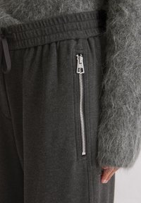 Donkergrijze joggers met een gestructureerde afwerking, voorzien van een ritszak aan de zijkant en een elastische tailleband voor een comfortabele pasvorm.