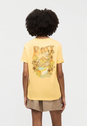 Isik, kellel on lokkis juuksed, kannab kollast T-särki, millel on lilleline, mägede ja jõe motiiv ning seljal tekst "ROXY 1990".