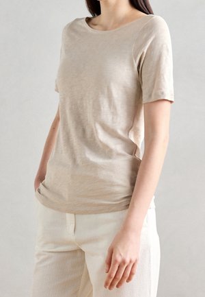 Beżowy t-shirt z krótkim rękawem, miękka faktura, zaokrąglony dekolt, luźny krój, zestawiony z kremowymi prążkowanymi spodniami, subtelnie casualowy design.