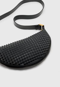 Svart lädercrossbodyväska med en texturerad pyramidal design, rund form och en tunn justerbar axelrem med detaljer i guld.