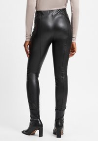 Leggings en simili cuir noir taille haute avec un ajustement près du corps, présentant des détails de couture et des accents zippés au niveau de la cheville. Texture lisse.