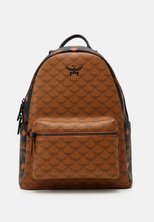 Sac à dos marron avec un motif texturé, doté d'une poche zippée à l'avant, d'accents noirs et d'un haut arrondi. Logo bien en vue sur le devant.