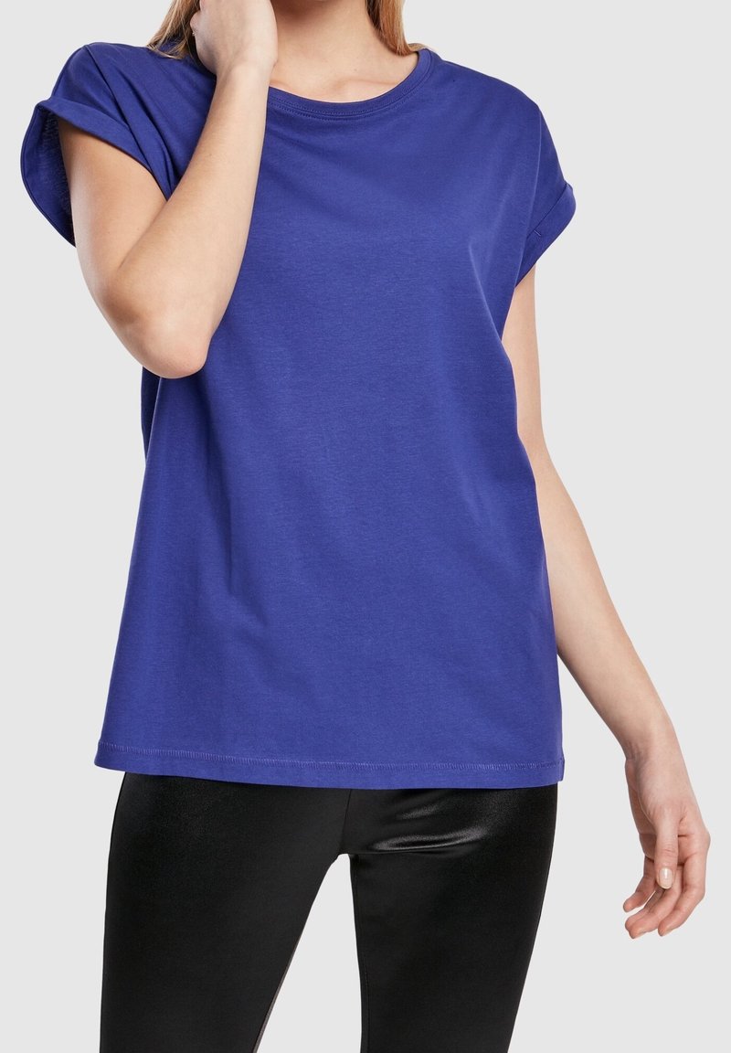 Lila bomullströja med uppvikta ärmar, rund halsringning och avslappnad passform. Kombinerad med svarta glänsande leggings.