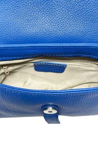 Inredning av en blå texturerad läderhandväska, med en dragkedjeficka och en mjuk beige foder, samt ett silverfärgat metallknäpp.