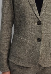 Grå och svart hounds-tooth kavaj gjord av texturerat tyg, med två knappar, slagkrage och två framfickor.