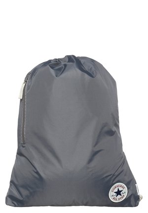 Mochila gris con cordón, bolsillo lateral con cremallera y un parche redondo con el logo de Converse All Star en la esquina inferior derecha.