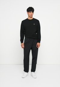 Black long-sleeve shirt with a small logo, paired with black elastic-waist pants featuring a subtle blue accent. White sneakers complete the outfit.