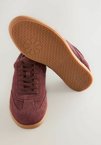 Burgundy suede sneakers with a rubber gum sole, featuring a textured pattern on the bottom and flat laces for secure fastening.