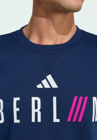 Navy blue sweatshirt with a round neckline, featuring white and pink graphic text "BERL" with three pink stripes, made from textured fabric.