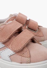 Pink suede shoes with Velcro straps, featuring a white leather accent. Rounded toe and textured surfaces. Rubber sole for stability.