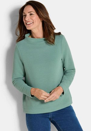 Pull-over vert menthe avec une texture côtelée, un large col et des manches longues, associé à un jean bleu. Design minimaliste, style décontracté.