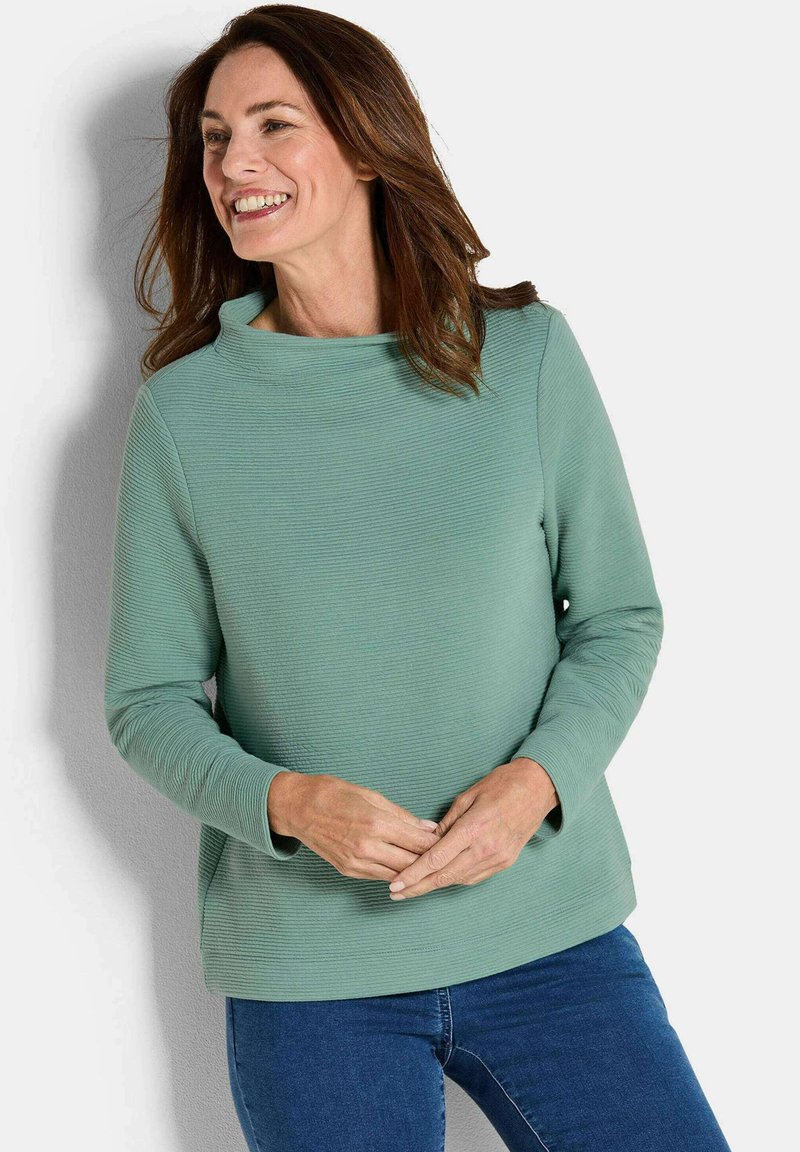 Mintgroene pullover met een geribbelde textuur, wijde halslijn en lange mouwen, gecombineerd met een blauwe jeans. Minimalistisch ontwerp, casual stijl.