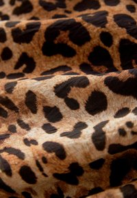 Tkanina s leopardím vzorom s jemnou textúrou na zlatohnedom pozadí a čiernymi nepravidelnými škvrnami, vytvárajúcimi jedinečný vzor.