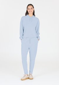 Helle blaue Kapuzenjacke mit Kordelzug und Kängurutasche, kombiniert mit passenden Sweatpants. Lässige Passform, weicher Stoff, elastischer Bund, legerer Look.