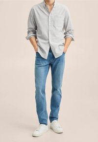 Gestreept overhemd in lichtgrijs en wit, gecombineerd met lichtblauwe spijkerbroeken en witte sneakers. Casual pasvorm met een zakdetail.