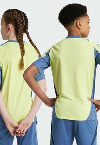 Deux enfants portent des maillots de sport assortis. Les tshirts sont d'un jaune clair avec des accents bleus, avec des manches courtes et une coupe décontractée.
