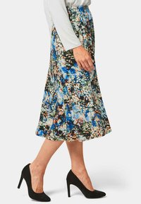 Floral Midirock in Schwarz, Blau und Orange mit elastischem Bund, fließendem Design und zarter Stoffstruktur. Kombiniert mit schwarzen Absätzen.