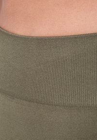 Olijfgroene ribgebreide tailleband en gladde stoftextuur, met een aansluitend ontwerp dat naadloos oogt en zonder zichtbare details.
