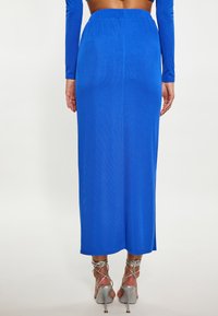 Blauwe geribbelde maxi rok met een elastische tailleband, gecombineerd met zilveren hoge hakken met strappy accenten. Glad textuur.