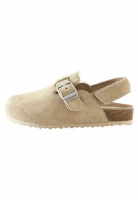 Sabot en suedine beige avec une boucle argentée réglable, un bout rond, une semelle en liège moulée et une semelle en caoutchouc avec un bord texturé.